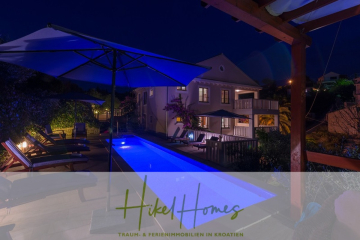 Eine moderne Villa in Kroatien bei Nacht mit einem blau beleuchteten Pool, Liegestühlen, Sonnenschirmen und üppiger Bepflanzung. Die Szene ist ruhig und einladend. Der Text "Hikel Homes - Traum- & Ferienimmobilien in Kroatien" erscheint am unteren Rand. - Villa mit 3 großzügigen Appartements mit jeweils 3 SZ, Küche, 2 x Pool, …
