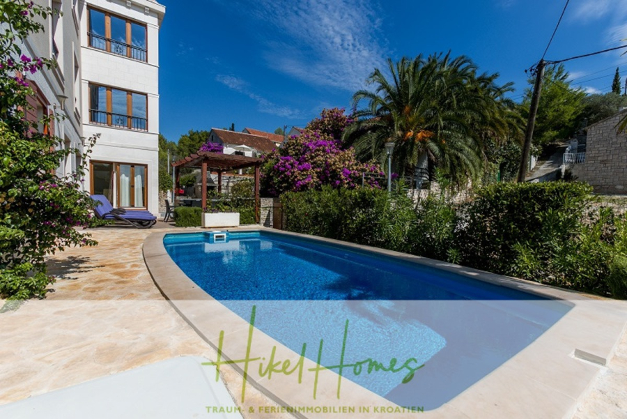 Villa mit 3 großzügigen Appartements mit jeweils 3 SZ, Küche, 2 x Pool, … - Eine moderne Villa mit privatem Außenpool, umgeben von üppigem Grün, Palmen und blühenden Blumen, unter einem klaren blauen Himmel; Sitzplätze auf der Terrasse sind in der Nähe des Hauses zu sehen. (46263)