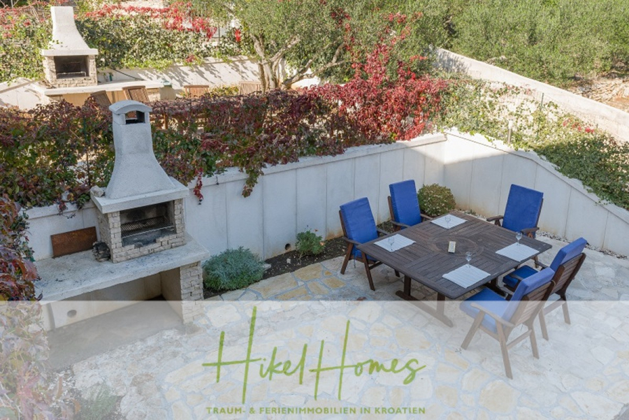 Villa mit 3 großzügigen Appartements mit jeweils 3 SZ, Küche, 2 x Pool, … - Steinterrasse im Freien mit einem großen Esstisch aus Holz und sechs blau gepolsterten Stühlen vor weißen, mit roten und grünen Ranken bewachsenen Wänden. Im Hintergrund sind zwei Steingrills zu sehen. (46269)