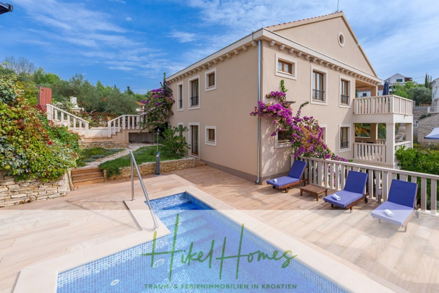 Villa mit 3 großzügigen Appartements mit jeweils 3 SZ, Küche, 2 x Pool, … - Eine moderne beigefarbene Villa mit Balkonen, lila Bougainvillea und einem kleinen Pool, umgeben von Liegestühlen und Grünpflanzen unter einem blauen Himmel. Der Schriftzug "Hikel Homes" ist am unteren Rand angebracht. (46261)