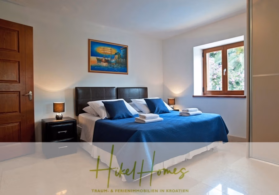 Villa mit 3 großzügigen Appartements mit jeweils 3 SZ, Küche, 2 x Pool, … - Ein helles Schlafzimmer mit zwei zusammengeschobenen Einzelbetten, blauen Tagesdecken und weißen Handtüchern. Zwei Nachttische mit schwarzen Lampen flankieren die Betten. Ein Fenster mit Gartenblick und einem gerahmten Meeresbild schmückt die Wand über den Betten. (41137)