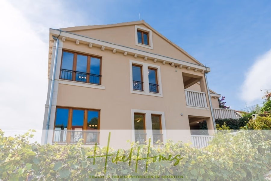 Villa mit 3 großzügigen Appartements mit jeweils 3 SZ, Küche, 2 x Pool, … - Ein beiges, mehrstöckiges Haus mit Holzfenstern und schrägem Dach, umgeben von Grün. Der Himmel ist klar und blau. Im unteren Drittel des Bildes ist eine Textüberlagerung mit den Worten „Hello Homes“ und einem deutschen Slogan zu sehen. (41133)