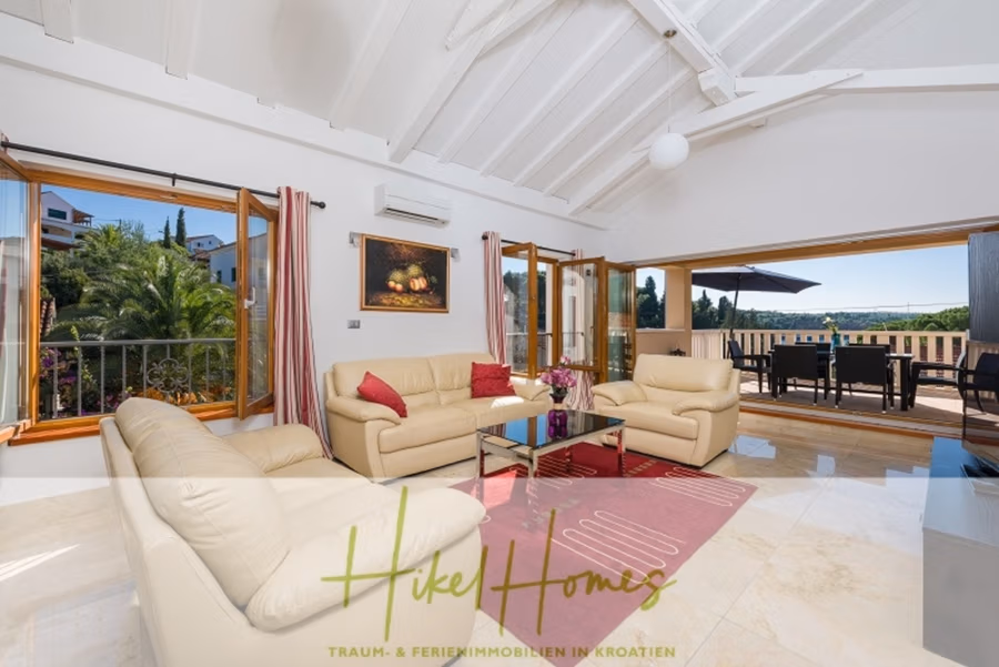 Villa mit 3 großzügigen Appartements mit jeweils 3 SZ, Küche, 2 x Pool, … - Geräumiges, luftiges Wohnzimmer mit cremefarbenen Ledersofas, einem Glas-Couchtisch auf einem roten Teppich und einem Flachbildfernseher. Große Fenster und Schiebetüren öffnen sich zu einem Balkon mit Sitzgelegenheiten im Freien und bieten einen Blick ins Grüne. Hohe Decken tragen zur Offenheit bei. (41147)