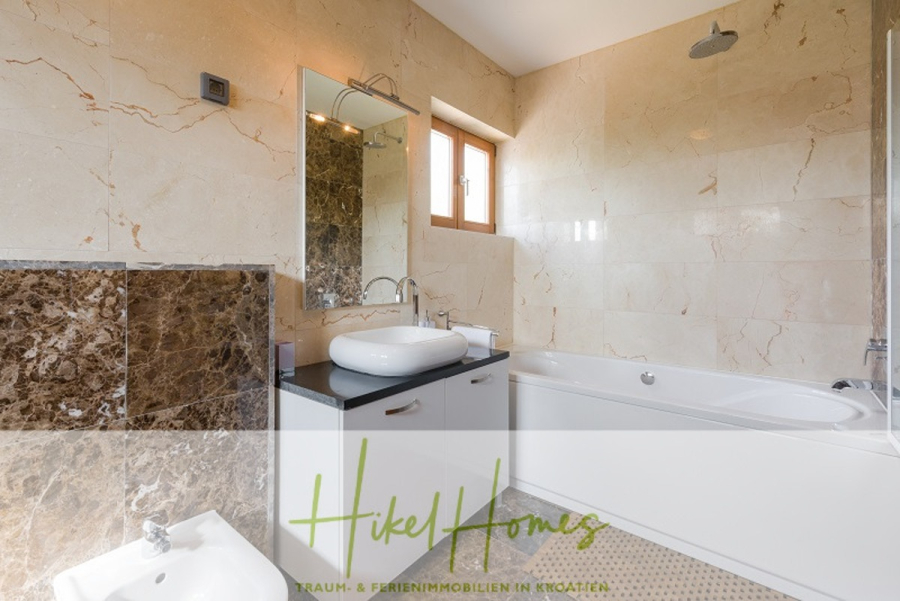 Villa mit 3 großzügigen Appartements mit jeweils 3 SZ, Küche, 2 x Pool, … - Modernes Badezimmer mit beigen Marmorwänden, einem großen Spiegel, einem weißen Waschbecken mit Schrank, einer Badewanne mit Duschkopf, einem Fenster und einer Teilansicht eines Bidets. Die Textüberlagerung lautet "Hikel Homes". (46275)