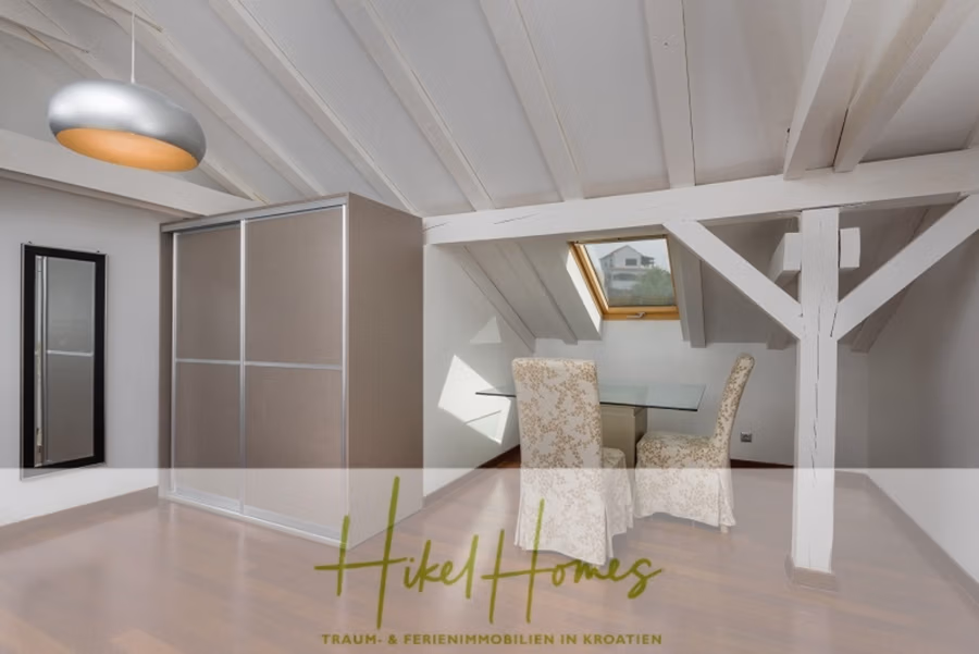 Villa mit 3 großzügigen Appartements mit jeweils 3 SZ, Küche, 2 x Pool, … - Dachzimmer mit Holzbalken und Dachschräge. Es verfügt über einen kleinen Esstisch mit zwei gemusterten Stühlen, einen Kleiderschrank mit Schiebetüren und ein Dachfenster. Der Boden ist aus Holz, und es gibt eine moderne Deckenleuchte. Unten steht der Markentext für Hikel Homes. (41149)