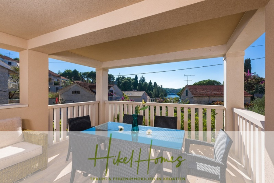 Villa mit 3 großzügigen Appartements mit jeweils 3 SZ, Küche, 2 x Pool, … - Eine überdachte Terrasse mit einem blauen Esstisch und Stühlen, einem Sofa und einer malerischen Aussicht auf Dächer und Grünflächen. Der Schriftzug "Hikel Homes" und "Traum & Ferienimmobilien in Kroatien" erscheint am unteren Rand. (46277)