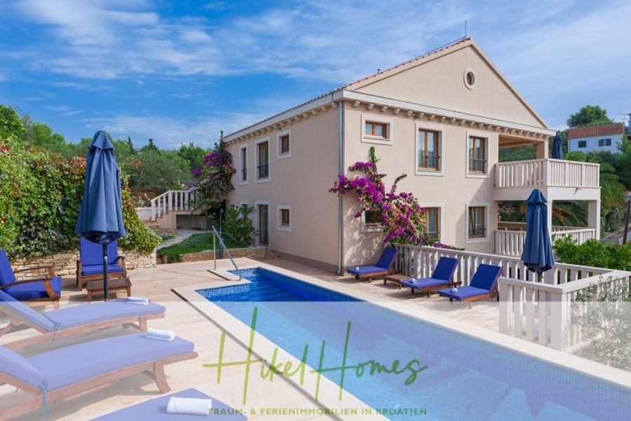 Villa mit 3 großzügigen Appartements mit jeweils 3 SZ, Küche, 2 x Pool, … - Eine moderne beigefarbene Villa mit Balkonen, umgeben von Grün und Blumen, verfügt über einen Pool mit blauen Liegestühlen und Sonnenschirmen daneben. Der Himmel ist klar und blau. Am unteren Rand des Bildes ist "Hike Homes" eingeblendet. (46256)