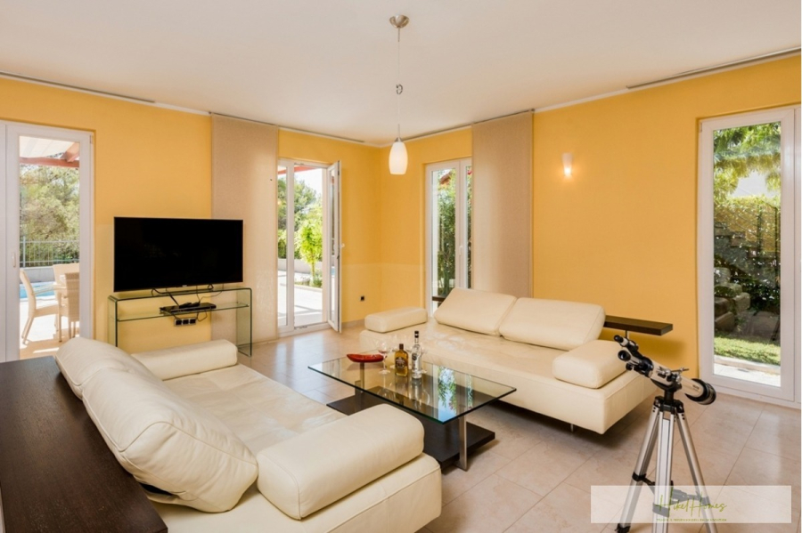 Großzügige Villa im Mittelmeerstil mit 3 SZ, Pool, Dachterrasse mit Meerblick (12) - Modernes Wohnzimmer mit gelben Wänden, weißen Ledersofas, einem Couchtisch aus Glas, einem Flachbildfernseher auf einem Glasständer und einem Fernrohr am Fenster. Große Fenster lassen natürliches Licht herein und bieten Ausblicke auf Grünflächen und einen Pool. (45887)