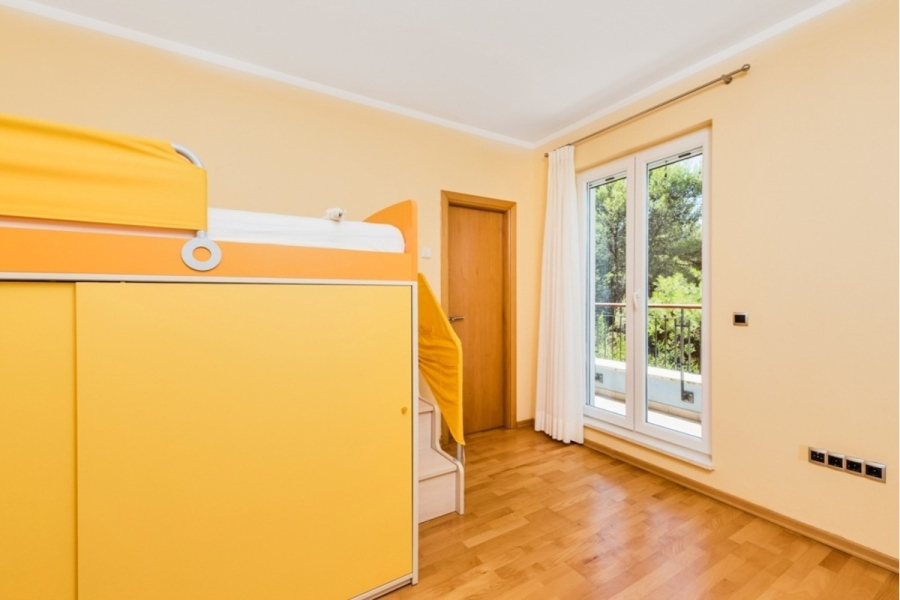 Großzügige Villa im Mittelmeerstil mit 3 SZ, Pool, Dachterrasse mit Meerblick (12) - Ein helles Schlafzimmer mit gelben Wänden verfügt über ein gelbes Etagenbett mit Stauraum und Treppe, Holzfußboden, eine Holztür und große Glastüren, die zu einem Balkon mit Grünflächen nach draußen führen. (45901)