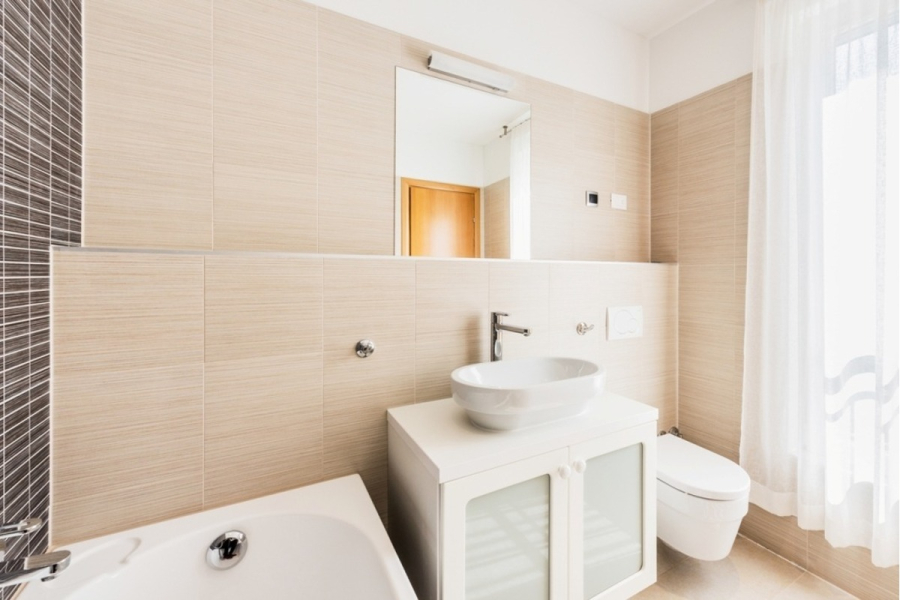 Großzügige Villa im Mittelmeerstil mit 3 SZ, Pool, Dachterrasse mit Meerblick (12) - Modernes Badezimmer mit beige gefliesten Wänden, einem weißen Waschbecken auf einem Schrank mit Milchglastüren, einer an der Wand befestigten Toilette, einer Badewannenecke, einem rechteckigen Spiegel und einem großen Fenster mit weißen, transparenten Vorhängen. (45903)