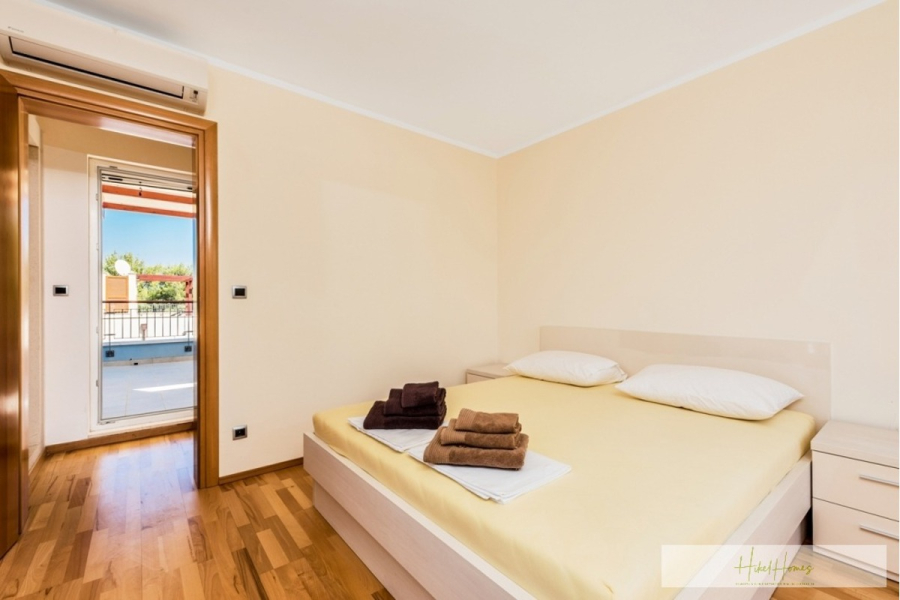 Großzügige Villa im Mittelmeerstil mit 3 SZ, Pool, Dachterrasse mit Meerblick (12) - Ein helles Schlafzimmer mit einem Doppelbett, zwei weißen Kissen, gefalteten Handtüchern auf dem Bett, hellem Holzfußboden, cremefarbenen Wänden, Klimaanlage und einer offenen Tür, die auf einen Balkon mit Sitzgelegenheiten im Freien führt. (45894)