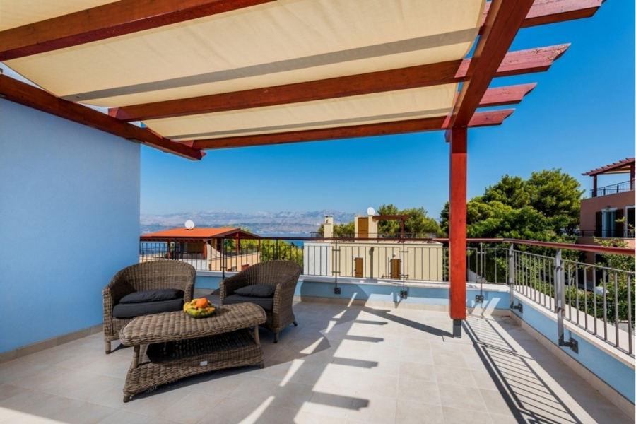 Großzügige Villa im Mittelmeerstil mit 3 SZ, Pool, Dachterrasse mit Meerblick (12) - Eine geräumige Terrasse mit Korbstühlen und einem Tisch unter einer hölzernen Pergola mit Sonnensegeln, mit Blick auf Gebäude, Bäume und einen fernen Blick auf das Meer unter einem klaren blauen Himmel. (45905)
