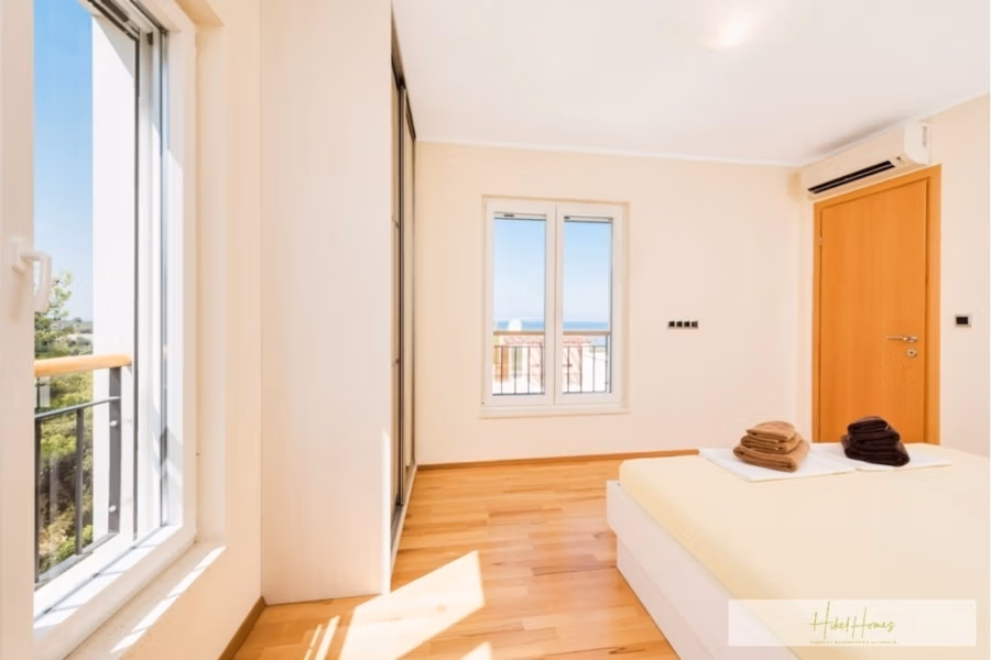 Großzügige Villa im Mittelmeerstil mit 3 SZ, Pool, Dachterrasse mit Meerblick (12) - Helles Schlafzimmer mit großem Fenster und Tür zum Balkon mit Meerblick. Das ordentlich gemachte Bett ist mit gefalteten Handtüchern ausgestattet. Das Zimmer verfügt über hellen Holzboden und eine Klimaanlage über der Tür. (42170)