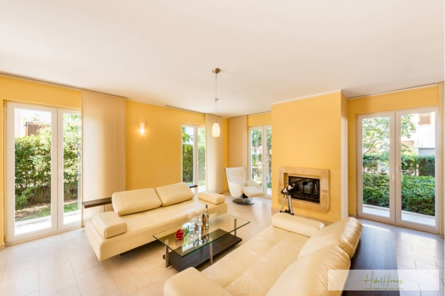 Großzügige Villa im Mittelmeerstil mit 3 SZ, Pool, Dachterrasse mit Meerblick (12) - Ein helles Wohnzimmer mit gelben Wänden, cremefarbenen Sofas, einem Couchtisch aus Glas, einem modernen Kamin und großen Fenstern, die natürliches Licht hereinlassen und den Blick ins Grüne freigeben. (45888)