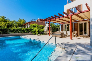 Ein modernes Haus mit einer Pergola-überdachten Terrasse, Sitzgelegenheiten im Freien und einem Essbereich neben einem klaren blauen Swimmingpool, umgeben von Grün unter einem strahlend blauen Himmel. - Großzügige Villa im Mittelmeerstil mit 3 SZ, Pool, Dachterrasse mit Meerblick (12)
