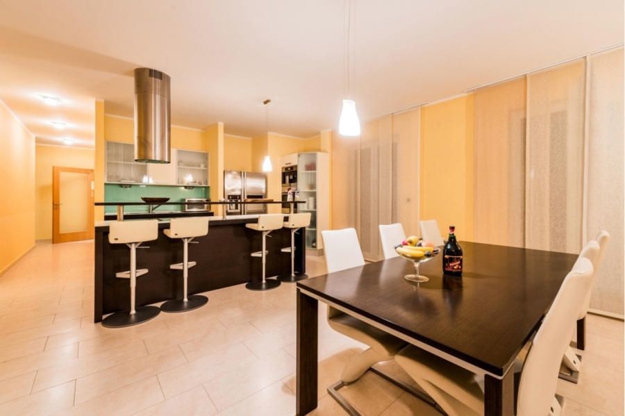 Großzügige Villa im Mittelmeerstil mit 3 SZ, Pool, Dachterrasse mit Meerblick (12) - Moderne Küche und Essbereich mit cremefarbenen Wänden, einem großen Esstisch aus dunklem Holz mit weißen Stühlen, einer Kücheninsel mit Barhockern, Geräten aus rostfreiem Stahl und Pendelleuchten. Eine Flasche und eine Obstschale stehen auf dem Tisch. (45897)