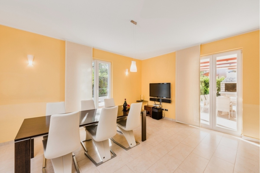 Großzügige Villa im Mittelmeerstil mit 3 SZ, Pool, Dachterrasse mit Meerblick (12) - Ein modernes Esszimmer mit hellgelben Wänden, einem dunklen rechteckigen Esstisch, sechs weißen Stühlen, einem Flachbildfernseher an der Wand und großen Fenstern, die viel Tageslicht hereinlassen. Durch Glastüren ist ein Innenhof mit Sitzgelegenheiten im Freien zu sehen. (45909)