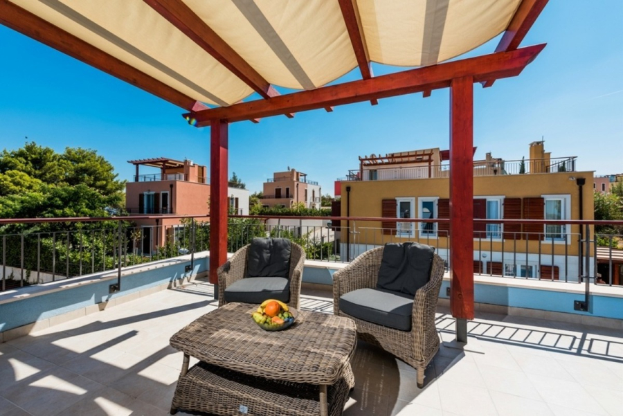 Großzügige Villa im Mittelmeerstil mit 3 SZ, Pool, Dachterrasse mit Meerblick (12) - Auf der Dachterrasse stehen zwei geflochtene Sessel mit Kissen und ein passender Tisch mit einer Schale Obst im Schatten einer hölzernen Pergola, mit Gebäuden und Bäumen im Hintergrund unter einem klaren blauen Himmel. (45906)