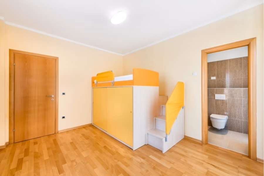 Großzügige Villa im Mittelmeerstil mit 3 SZ, Pool, Dachterrasse mit Meerblick (12) - Ein helles, minimalistisches Zimmer mit Holzboden und einem Hochbett in Orange-Gelb-Farben. Es verfügt über eine eingebaute Treppe und Stauraum. Die Tür führt zu einem kleinen Badezimmer mit hellbraunen Fliesen und einer weißen Toilette. (42176)