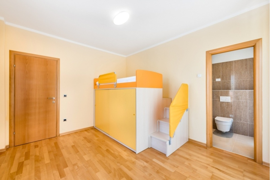 Großzügige Villa im Mittelmeerstil mit 3 SZ, Pool, Dachterrasse mit Meerblick (12) - Ein helles, modernes Zimmer mit hellem Holzboden, einer Holztür, einem Etagenbett mit gelben Akzenten und eingebautem Stauraum, einer weißen Treppe und einer offenen Tür, die zu einem Badezimmer mit braunen Fliesenwänden und einer Toilette führt. (45902)