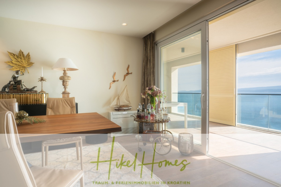 MEERBLICK & KUNST Designer Luxus Appartement mit 3 Schlafzimmer – großer Loggia - Modernes Esszimmer mit Holztisch und stilvollem Dekor, das sich zu einem sonnigen Balkon mit Glastüren und Panoramablick auf das Meer öffnet. Der Schriftzug "Hikel Homes" ist am Boden eingeblendet. (45387)