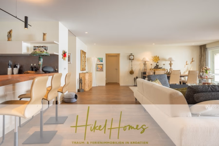 MEERBLICK & KUNST Designer Luxus Appartement mit 3 Schlafzimmer – großer Loggia - Modernes Wohnzimmer mit offenem Grundriss. Links befindet sich ein Barbereich mit Hockern, rechts eine gemütliche Sitzecke mit einem beigen Sofa. Der Raum verfügt über Holzböden, modernes Dekor und große Fenster, die viel Tageslicht hereinlassen. (41089)