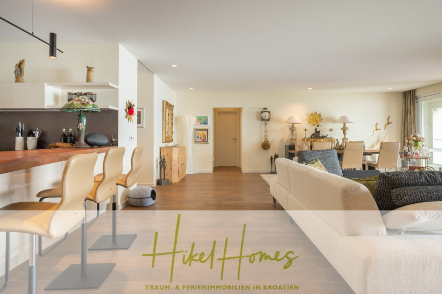 MEERBLICK & KUNST Designer Luxus Appartement mit 3 Schlafzimmer – großer Loggia - Moderner, geräumiger Wohnbereich mit hellen Sofas, Barhockern am Küchentresen, Holzböden und geschmackvollem Dekor. Große Fenster lassen viel natürliches Licht herein. Unten ist "Hikel Homes - Traum- & Ferienimmobilien in Kroatien" eingeblendet. (45395)