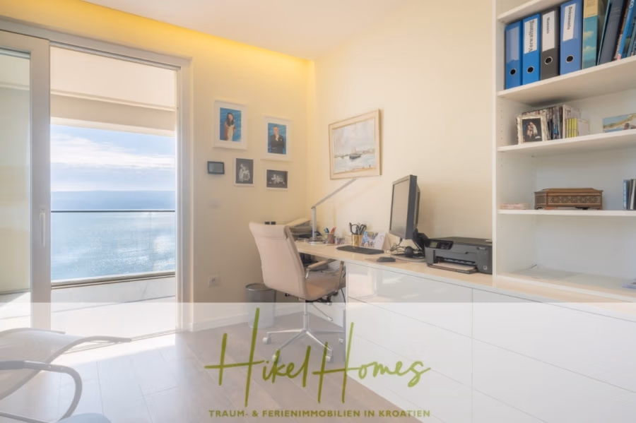 MEERBLICK & KUNST Designer Luxus Appartement mit 3 Schlafzimmer – großer Loggia - Ein helles und modernes Homeoffice mit großem Schreibtisch und Computer, Bücherregalen mit Ordnern und Büchern sowie Blick aufs Meer durch eine Glastür. Die Wände sind mit Gemälden geschmückt. Unten steht: „Hikel Homes – Traum- & Ferienimmobilien in Kroatien.“. (41076)