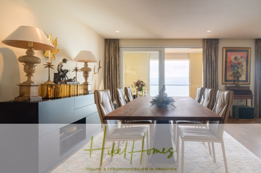 MEERBLICK & KUNST Designer Luxus Appartement mit 3 Schlafzimmer – großer Loggia - Ein Esszimmer mit einem langen Holztisch und weißen Stühlen. Ein Sideboard mit kunstvollen Lampen und einer kleinen Skulptur. Eine Glasschiebetür gibt den Blick aufs Meer frei. Rechts stehen ein gerahmtes Kunstwerk und eine Topfpflanze. Text: „HikeHomes“. (41087)