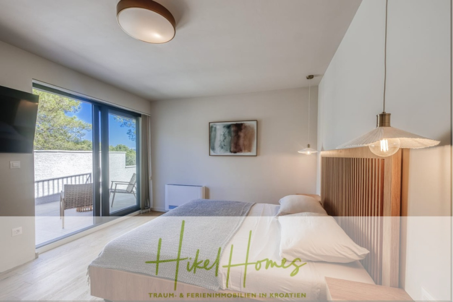 Moderne Meerblick Villa mit Infinity-Pool, Bootsanleger, 100m zum Meer - Ein modernes Schlafzimmer mit einem großen Bett, minimalistischer Einrichtung und einer Glasschiebetür, die auf einen Balkon mit Sitzgelegenheiten im Freien führt. Das Sonnenlicht erhellt den Raum, und der Text "Hikel Homes" erscheint am unteren Rand. (44441)