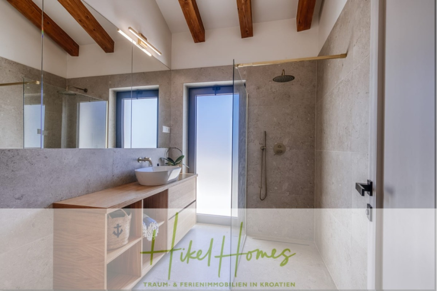 Moderne Meerblick Villa mit Infinity-Pool, Bootsanleger, 100m zum Meer - Modernes Badezimmer mit hölzernem Waschtisch, Gefäßwaschbecken, Spiegel, begehbarer Dusche und Glastür; freiliegende Holzbalken an der Decke sorgen für Wärme. Der Logo-Text unten lautet "Vikel Homes - Traum- & Ferienimmobilien in Kroatien. (44447)