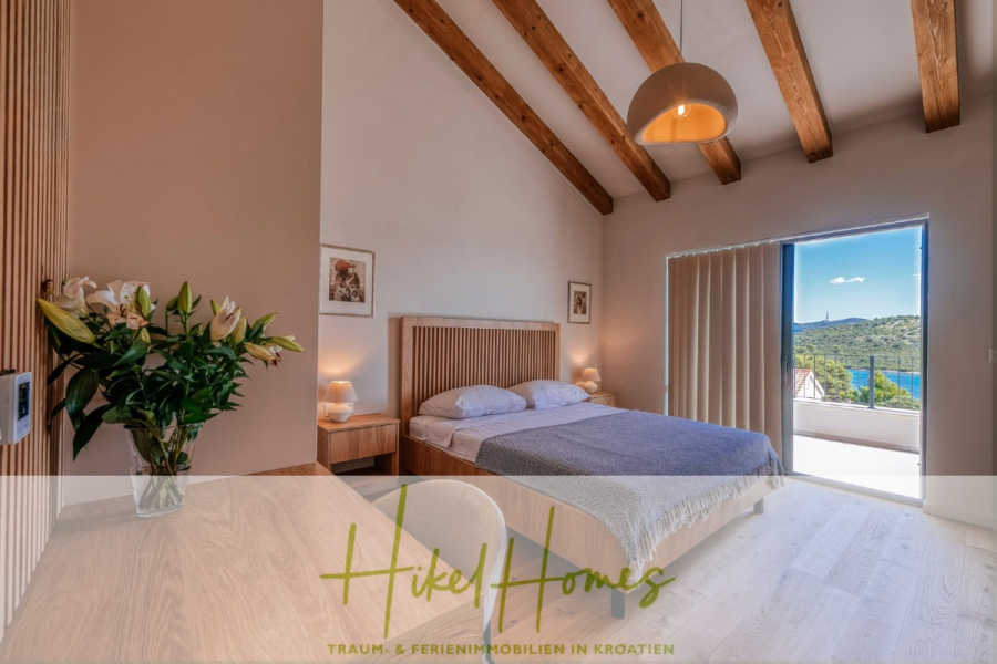 Moderne Meerblick Villa mit Infinity-Pool, Bootsanleger, 100m zum Meer - Ein modernes Schlafzimmer mit einem Holzbett, Nachttischen, Blumen und sichtbaren Holzbalken an der Decke. Große Glastüren führen auf einen Balkon mit Blick auf die Hügel und den blauen Himmel. (44451)