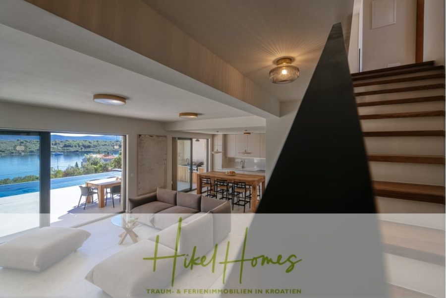 Moderne Meerblick Villa mit Infinity-Pool, Bootsanleger, 100m zum Meer - Modernes Wohnzimmer mit großen Fenstern und freiem Blick auf einen Pool und Wasser, neben einem Essbereich und einer Küche. Eine Holztreppe führt in die obere Etage. Textüberlagerung lautet "Hikel Homes: Traum- & Ferienimmobilien in Kroatien. (44439)