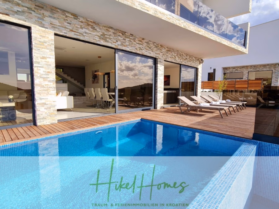 Seeview 2 von 3 | Möbilierte Luxus-Meerblick Villa mit 4 SZ, Pool, Sauna, Fitness, Jacuzzi, - Luxuriöse, moderne Villa mit Steinakzenten, Glaswänden, offenem Wohnbereich und großzügiger Holzterrasse mit Liegestühlen am Pool. Der Himmel spiegelt sich in den Fenstern und im Wasser und schafft eine ruhige Atmosphäre. Schild: „Hikel Homes“. (41753)