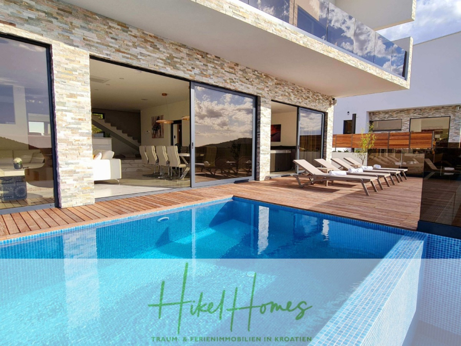 Seeview 2 von 3 | Möbilierte Luxus-Meerblick Villa mit 4 SZ, Pool, Sauna, Fitness, Jacuzzi, - Moderne Villa mit Steinfassade, Glastüren, Liegestühlen auf einer Holzterrasse und einem blauen Swimmingpool. Auf den Fenstern sind Spiegelungen von Wolken zu sehen. Der Schriftzug "Hikel Homes" erscheint am unteren Rand. (45603)