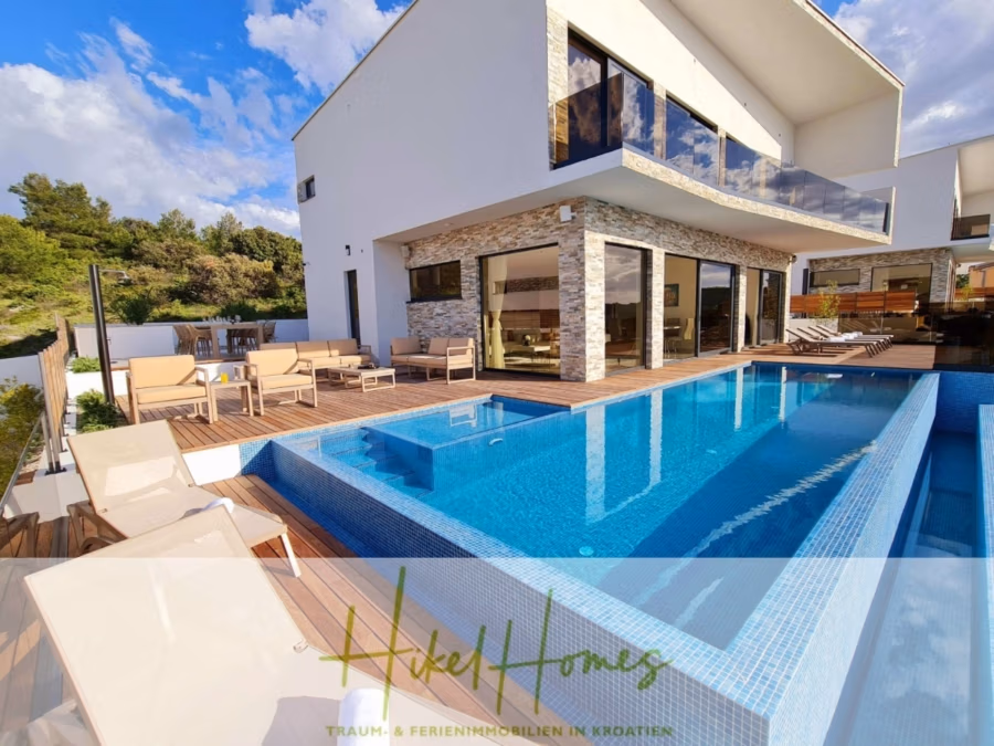 Seeview 2 von 3 | Möbilierte Luxus-Meerblick Villa mit 4 SZ, Pool, Sauna, Fitness, Jacuzzi, - Moderne Villa mit Steinakzenten und großen Fenstern, Infinity-Pool und Holzterrasse. Umgeben von Liegestühlen und viel Grün bietet die Villa einen Blick auf eine malerische Hügellandschaft unter leicht bewölktem Himmel. (41761)