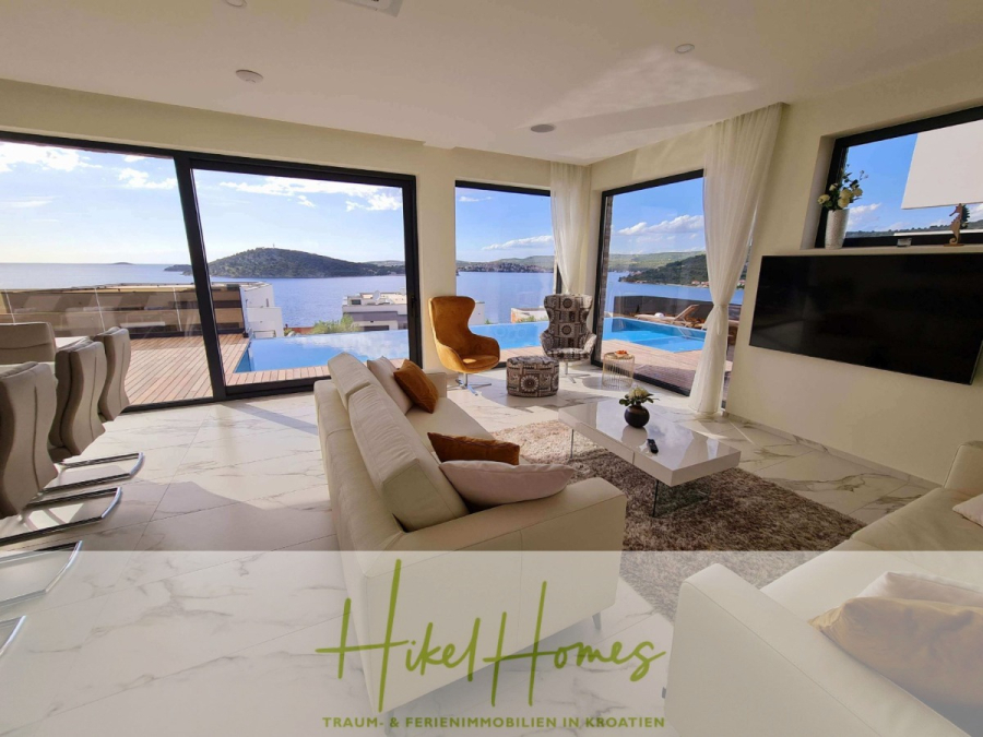 Seeview 2 von 3 | Möbilierte Luxus-Meerblick Villa mit 4 SZ, Pool, Sauna, Fitness, Jacuzzi, - Modernes Wohnzimmer mit großen Fenstern mit Blick auf das Meer, einem Pool auf der Terrasse, stilvollen Möbeln und einfallendem Sonnenlicht. Logo und Text "Hikel Homes - Traum & Ferienimmobilien in Kroatien" am unteren Rand. (45609)