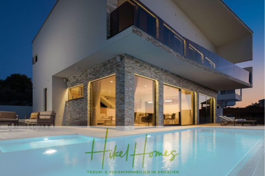 Seeview 2 von 3 | Möbilierte Luxus-Meerblick Villa mit 4 SZ, Pool, Sauna, Fitness, Jacuzzi, - Moderne zweistöckige Villa mit großen Glasfenstern, Steinakzenten und einem in der Abenddämmerung leuchtenden Außenpool. Auf dem Pooldeck sind Liegestühle aufgestellt. Das Logo "Hikel Homes" ist am unteren Rand eingeblendet. (45593)