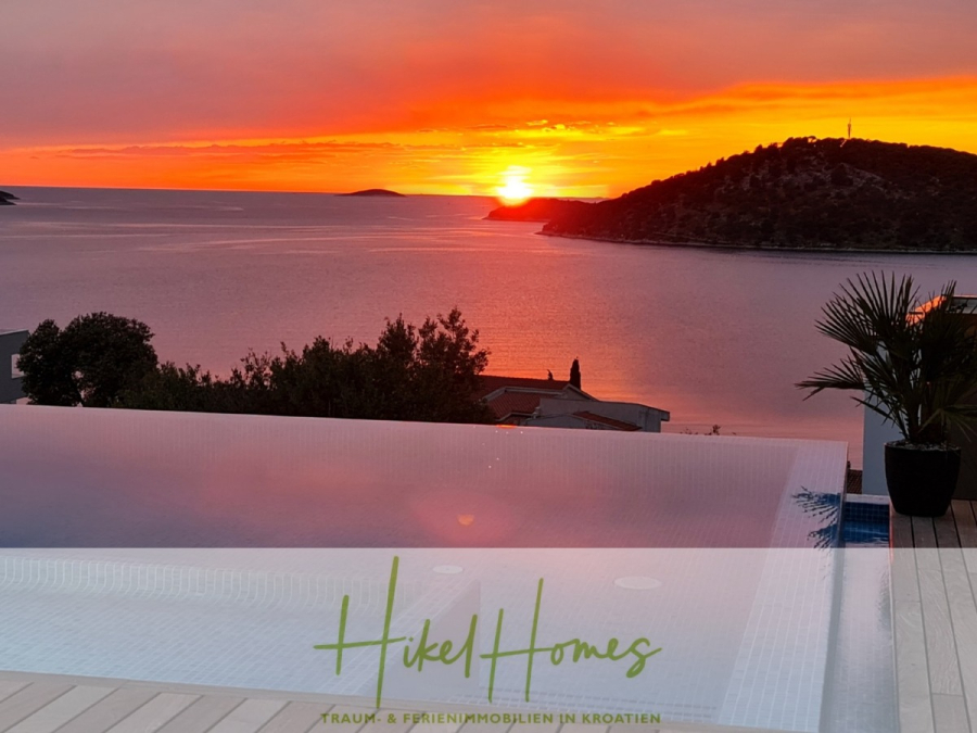 Seeview 2 von 3 | Möbilierte Luxus-Meerblick Villa mit 4 SZ, Pool, Sauna, Fitness, Jacuzzi, - Infinity-Pool mit Blick auf ein ruhiges Meer bei Sonnenuntergang, mit leuchtend orangefarbenem und rotem Himmel, silhouettierten Bäumen, kleinen Inseln und der hinter einem Hügel untergehenden Sonne. Die Textüberlagerung unten lautet "Hikel Homes". (45599)