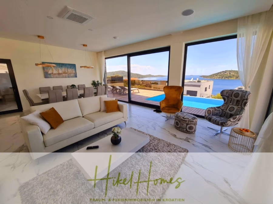 Seeview 2 von 3 | Möbilierte Luxus-Meerblick Villa mit 4 SZ, Pool, Sauna, Fitness, Jacuzzi, - Luxuriöses Wohnzimmer mit modernen Möbeln, darunter ein weißes Sofa und gemusterte Stühle, mit Blick auf den Pool und den malerischen Meerblick durch große Fenster. Essbereich auf der linken Seite. Hell und geräumig mit elegantem Dekor. (41759)