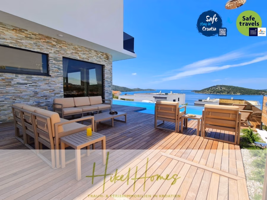 Seeview 2 von 3 | Möbilierte Luxus-Meerblick Villa mit 4 SZ, Pool, Sauna, Fitness, Jacuzzi, - Eine moderne Außenterrasse mit Holzbelag und malerischem Meerblick. Sie verfügt über beigefarbene Polsterstühle, ein Sofa und einen Couchtisch mit einem Glas und einem Snack. Der klare und helle Himmel unterstreicht die entspannte Küstenatmosphäre. (41746)