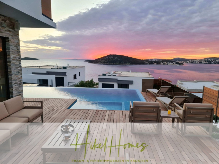 Seeview 2 von 3 | Möbilierte Luxus-Meerblick Villa mit 4 SZ, Pool, Sauna, Fitness, Jacuzzi, - Moderne Terrasse mit Pool und Blick auf das Meer bei Sonnenuntergang, mit Sitzgelegenheiten im Freien, einem Tisch mit Getränken und Blick auf Inseln und den bunten Himmel. Der Schriftzug "Hikel Homes" erscheint am unteren Rand des Bildes. (45595)