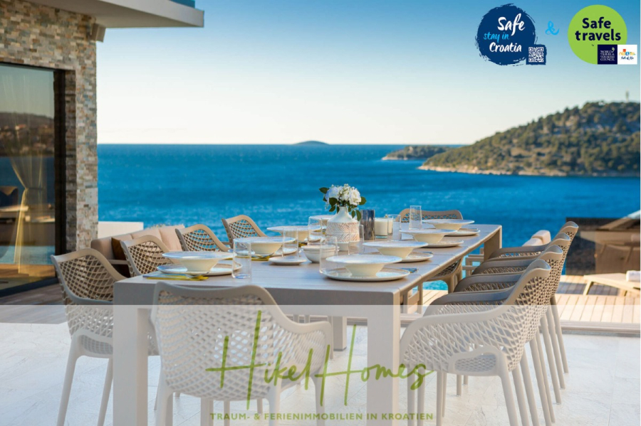 Seeview 2 von 3 | Möbilierte Luxus-Meerblick Villa mit 4 SZ, Pool, Sauna, Fitness, Jacuzzi, - Ein moderner Esstisch für zwölf Personen im Freien bietet einen herrlichen Blick auf das blaue Meer und die Hügel. Die Umgebung ist stilvoll und einladend, mit Sicherheitsplaketten und dem Branding "Hikel Homes". (45591)