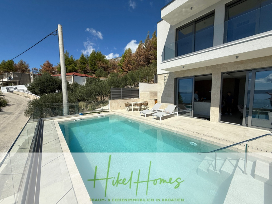 Erstbezug – ab sofort und Herbst genießen! Schlüsselfertige Meerblick Villa, 3SZ, Pool, … - Moderne weiße Villa mit großen Glastüren, privatem Pool und Liegestühlen an einem sonnigen Tag; umgeben von Bäumen und einem blauen Himmel. Der Text "Hikel Homes" und Details über Immobilien in Kroatien erscheinen am unteren Rand. (44477)