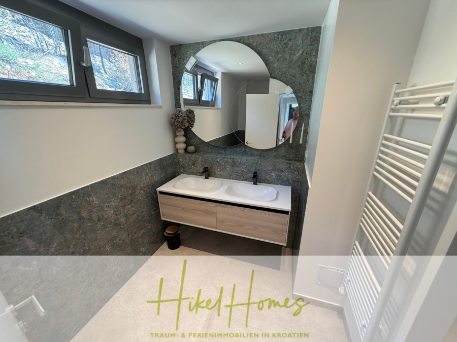 Erstbezug – ab sofort und Herbst genießen! Schlüsselfertige Meerblick Villa, 3SZ, Pool, … - Modernes Badezimmer mit Doppelwaschbecken, großem Spiegel, zwei schwarzen Wasserhähnen, Handtuchheizkörper und Fenster über dem Waschbecken. Es gibt eine dekorative Vase auf der Theke und natürliches Licht einfällt. (44488)