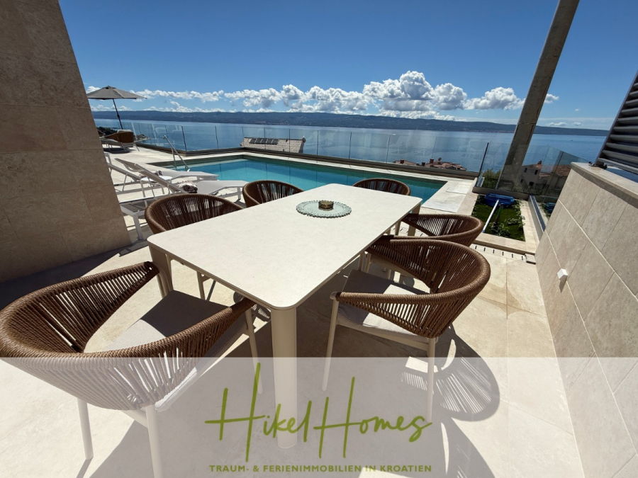 Erstbezug – ab sofort und Herbst genießen! Schlüsselfertige Meerblick Villa, 3SZ, Pool, … - Ein sonnenbeschienener Essbereich im Freien mit Korbstühlen und einem Tisch blickt auf einen Swimmingpool und das Meer, mit klarem Himmel und Wolken in der Ferne. Der Text am unteren Rand lautet "Hikel Homes Traum- & Ferienimmobilien in Kroatien. (44479)