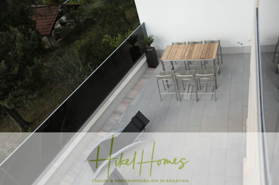 Erstbezug-Neubau Villa / Luxus Ausstattung / Pool / … - Ein moderner Balkon mit einem Holztisch, sechs Metallstühlen und zwei Loungesesseln bietet einen Blick auf eine grüne Landschaft. Der Boden ist gefliest und es gibt ein Glasgeländer. Der Text "Hikel Homes" erscheint am unteren Rand. (45942)