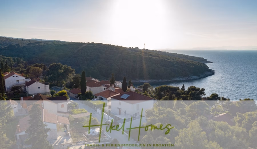 Erstbezug-Neubau Villa / Luxus Ausstattung / Pool / … - Luftaufnahme eines ruhigen Küstendorfes bei Sonnenuntergang. Häuser mit roten Dächern liegen eingebettet in üppiges Grün nahe dem Wasser. Ein bewaldeter Hügel erstreckt sich bis ins Meer, in der Ferne ragt ein Leuchtturm empor. Die Sonne taucht die ruhige Szenerie in ein warmes Licht. (42534)