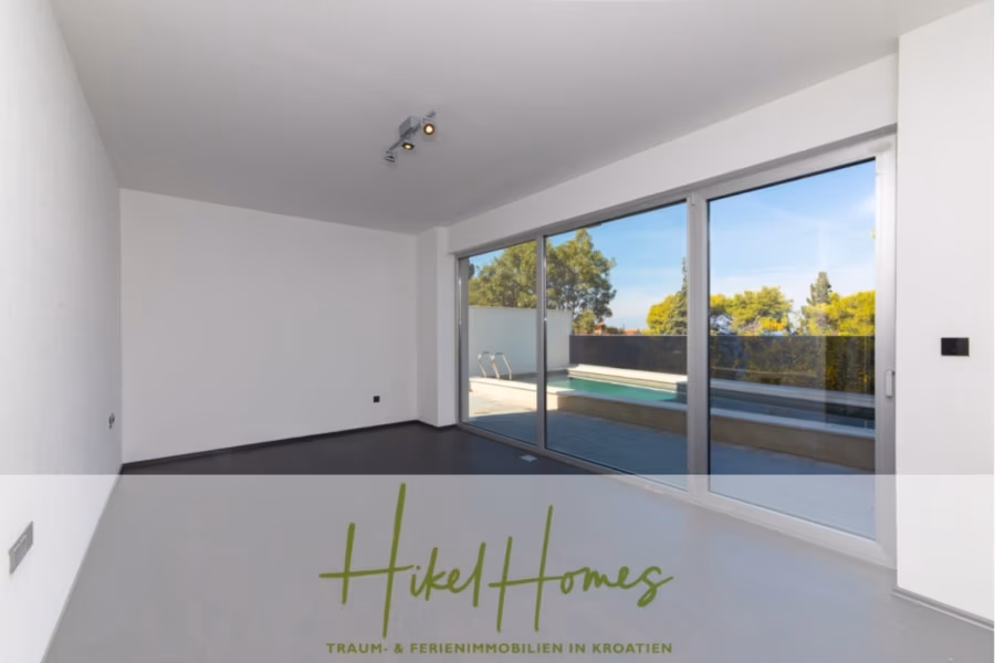 Erstbezug-Neubau Villa / Luxus Ausstattung / Pool / … - Geräumiger, leerer Raum mit grauem Boden und weißen Wänden. Große Glastüren führen auf einen Balkon mit Poolblick. Die Szenerie umfasst Bäume und einen strahlend blauen Himmel. Textüberlagerung: „Hikel Homes – Traum- & Ferienimmobilien in Kroatien.“. (42537)