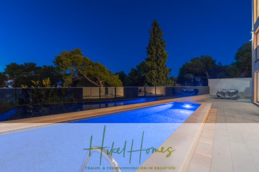 Erstbezug-Neubau Villa / Luxus Ausstattung / Pool / … - Ein moderner Außenpool, nachts beleuchtet, umgeben von Bäumen. Der Himmel ist klar, und in der Einfahrt steht ein überdachtes Auto. Das Bild enthält den Text: „Hikel Homes“ und „Traum- & Ferienimmobilien in Kroatien“. (42542)